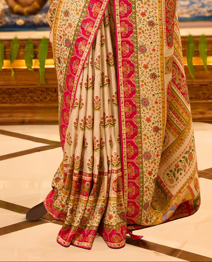 Ivory colour Pashmina silk saree richly adorned with intricate multicolour floral motifs across the body, accentuated by vibrant pink and green ornamental borders and a grand storytelling pallu, beautifully paired with a matching blouse piece.
