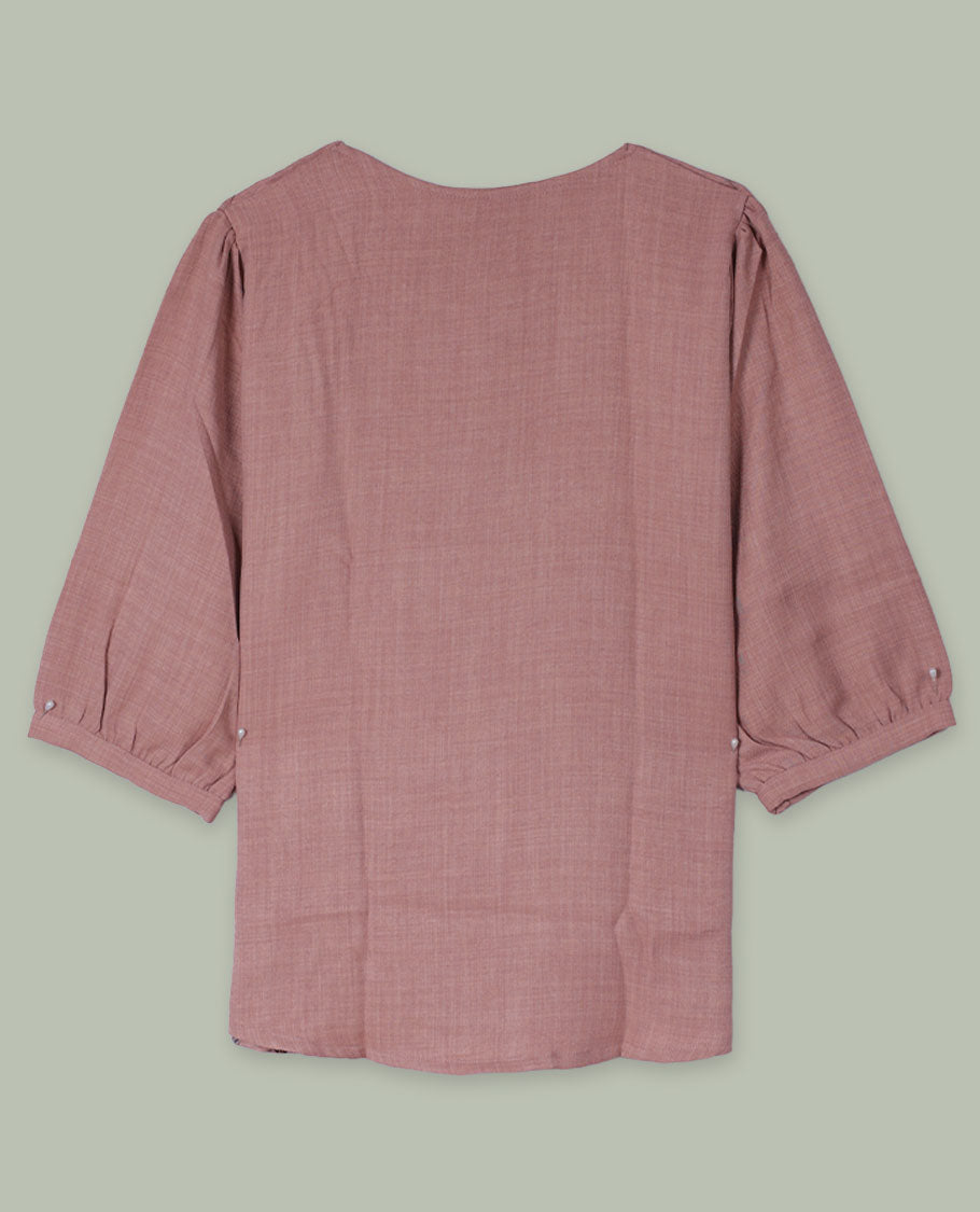 Dusty rose round-neck top with three-quarter sleeves and placement floral print in muted blue, green, and burgundy tones along the front hem and side.