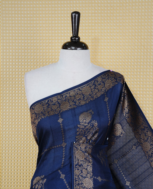 Navy blue colour semi banaras tussar georgette saree featuring gold zari floral pattern body, finished with gold zari floral motifs on border and paired with matching blouse piece.