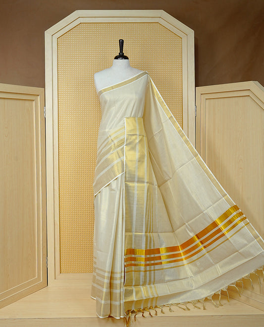 Cream Colour Tissue Kerala Saree Featuring A Classy Plain Body, Beautifully Enhanced With A Traditional Gold Zari Striped Border And Rich Gold Zari Pallu, Finished With Elegant Tassels, Paired With A Matching Blouse Piece.