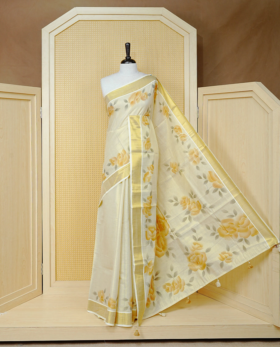 Cream Colour Tissue Kerala Saree Featuring Digital Mustard Yellow Rose Prints Across The Body, Enhanced With A Gold Zari Border , Finished With Light Brown & Cream Tassels And A Matching Blouse Piece