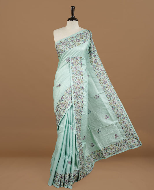 Mint colour Semi Tussar silk saree features an intricate, multi colored Kashmiri Kashida style floral embroidered border and scattered motifs, paired with a matching unstitched blouse piece.