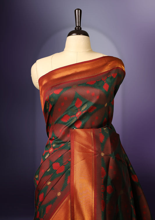 Maroon and green Ikat silk saree featuring intricate woven geometric and floral motifs across the body and pallu, complemented with a golden brown zari border and tassels, paired with a matching blouse piece.