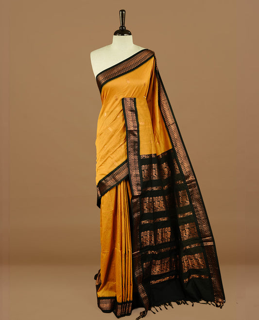 Mustard colour kalyani cotton saree featuring gold zari motifs on body, highlighting contrast Black colour with Antique gold zari border, paired with matching blouse piece.