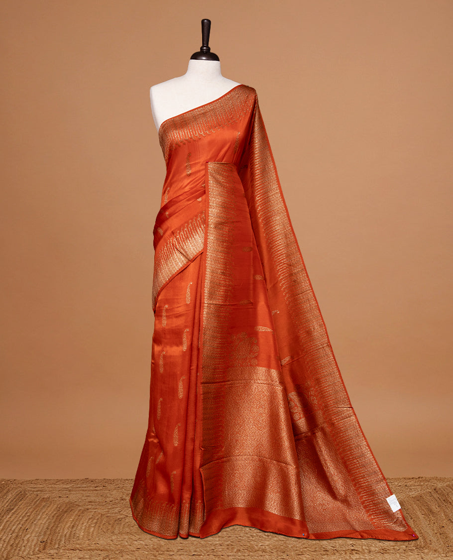 Burnt Orange colour Semi Banaras Tussar Georgette Featuring Gold zari Leaf pattern on body, Finished with Gold zari border and paired with matching blouse piece.