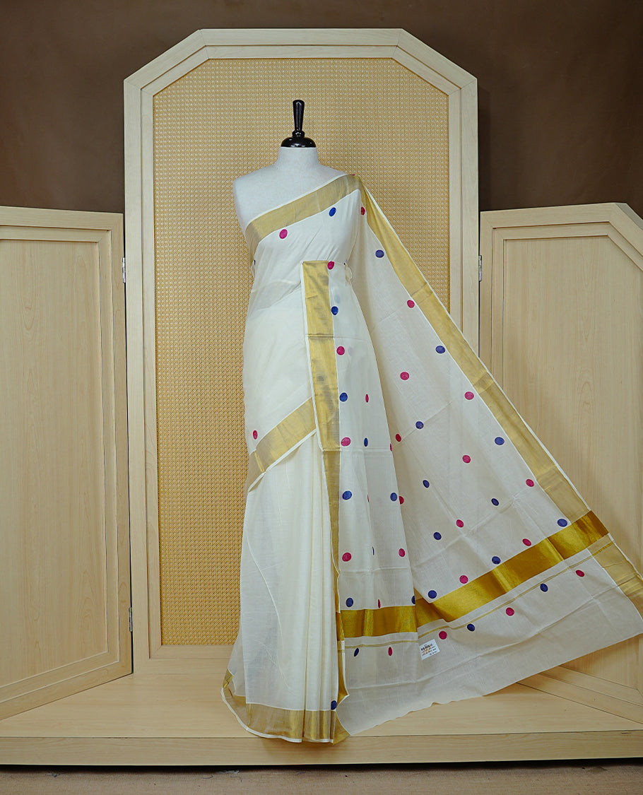 Cream Colour cotton Kerala Saree Featuring  Magenta & Blue Dot Prints On The Body, Complemented By A Traditional Gold Zari Border, Paired With A Matching Blouse Piece.