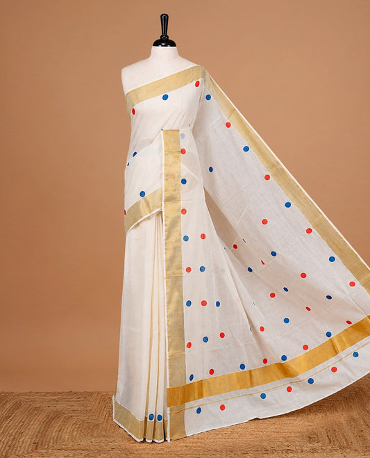Cream Colour cotton Kerala Saree Featuring Multicolour Dot Prints On The Body, Complemented By A Traditional Gold Zari Border, Paired With A Matching Blouse Piece.