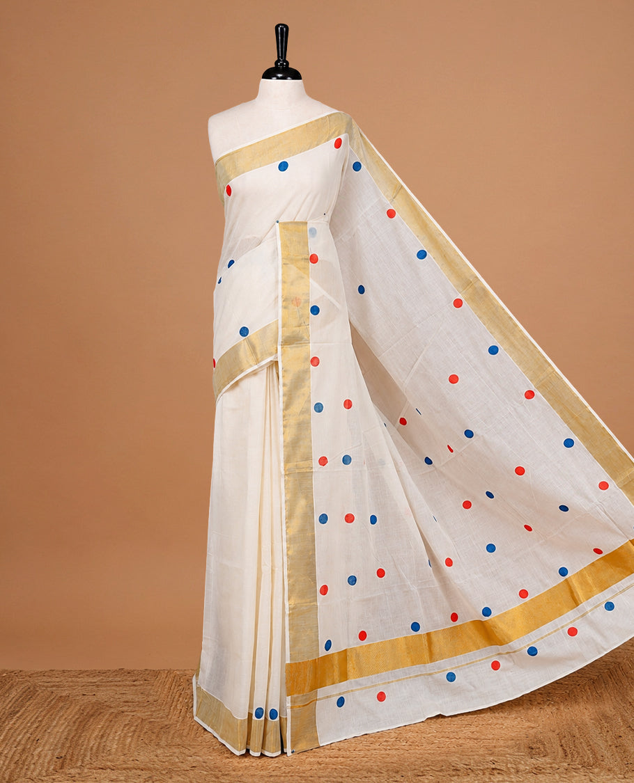 Cream Colour cotton Kerala Saree Featuring Multicolour Dot Prints On The Body, Complemented By A Traditional Gold Zari Border, Paired With A Matching Blouse Piece.