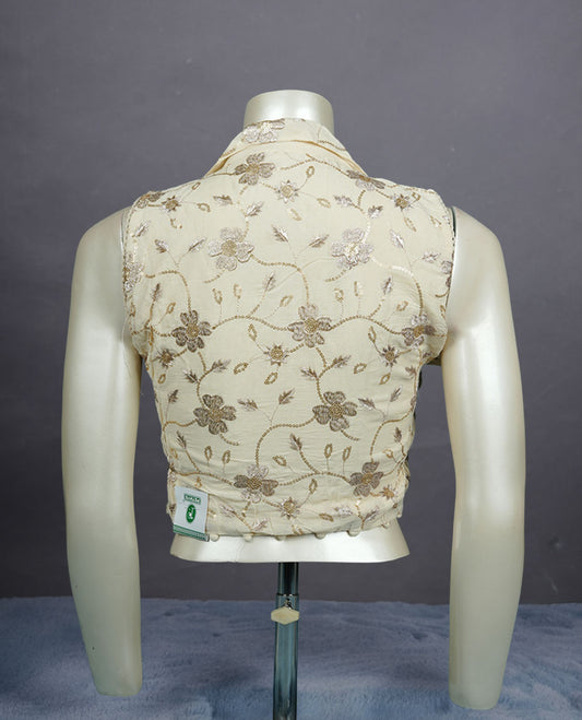Cream embroidered sleeveless blouse with delicate floral threadwork, front buttons, and soft pom-pom hem detailing.