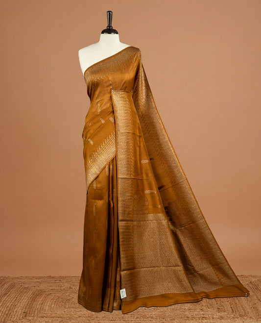 Dark Mustard colour Semi Banaras Tussar Georgette Featuring Gold zari Leaf pattern on body, Finished with Gold zari border and paired with matching blouse piece.