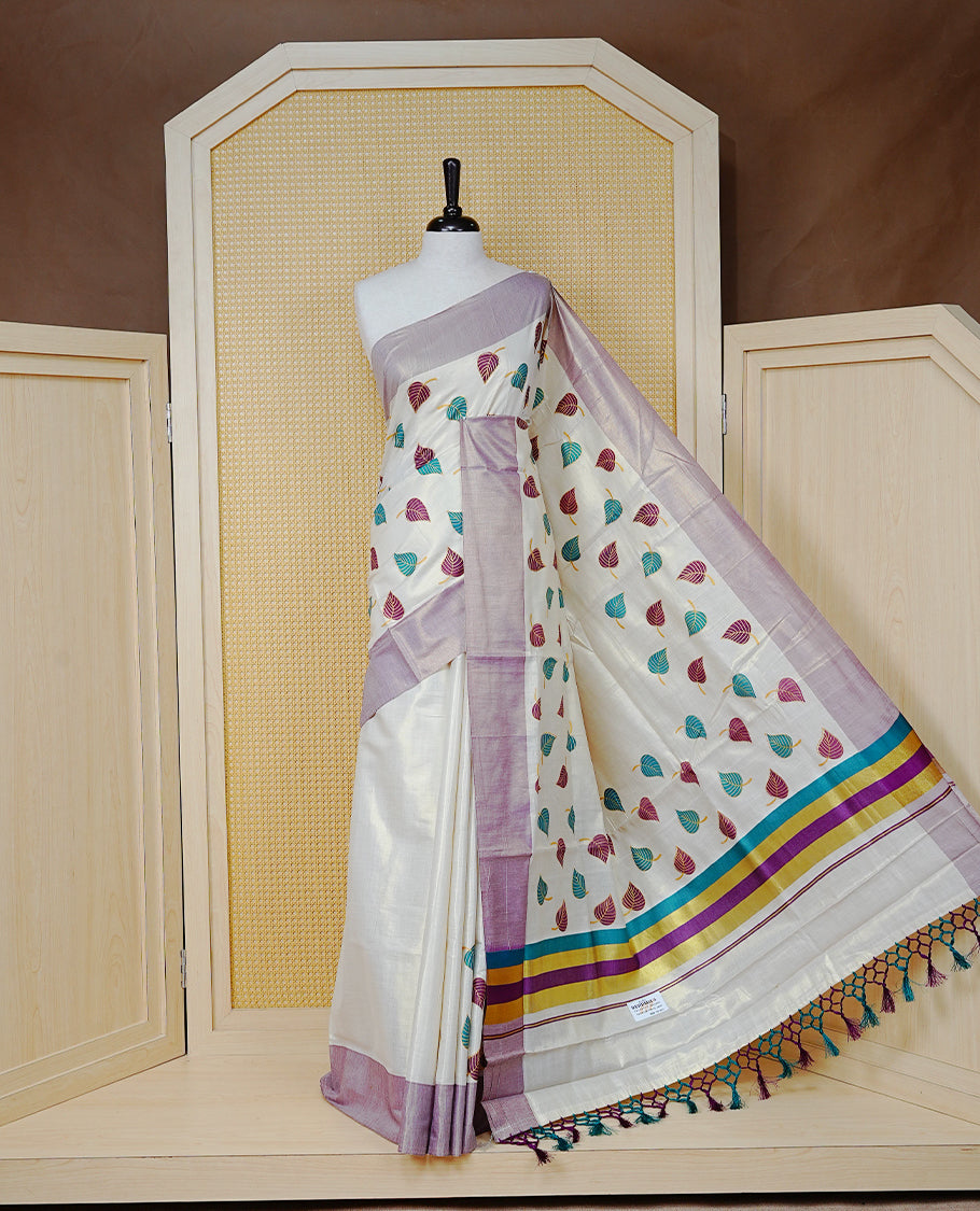 Cream Colour Tissue Kerala Saree Featuring Green and Brown Leaf Prints Across the Body, Enhanced with a Gold Zari, Purple and Green Border & Pallu, Green  and Purple  Tassels, and a Matching Blouse Piece.
