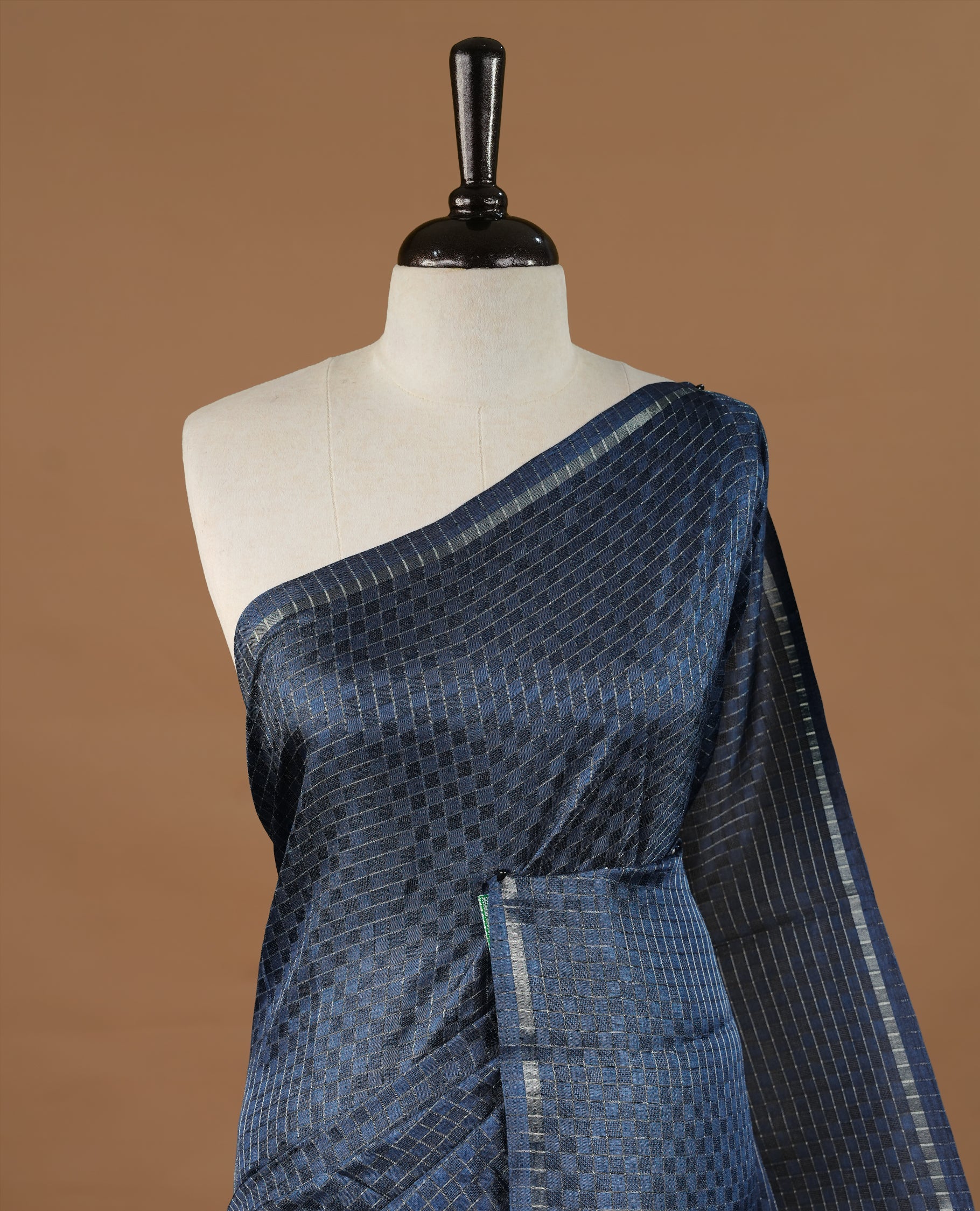 Navy Blue colour Semi Tussar saree featuring an elegant zari fancy check pattern on the body, highlighted with a small border for a refined look. Comes without a blouse piece.