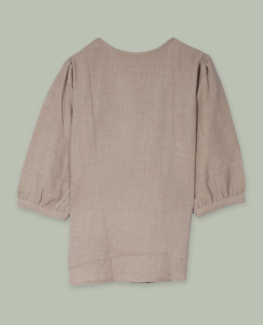 Beige round-neck top with elbow-length sleeves and placement floral print in muted blue, green, and rose tones along the front hem and side.