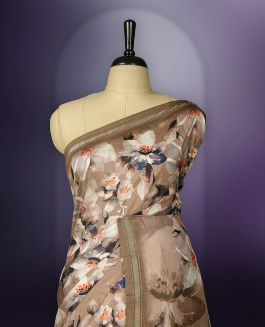 Pastel brown colour saree adorned with elegant floral prints on the body, enhanced with a subtle matching border, complemented by a beautifully printed pallu featuring blooming flowers, and paired with a matching blouse.