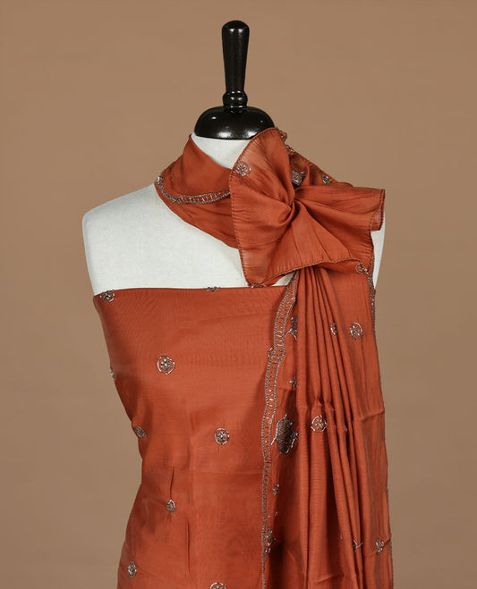 Brick orange colour churidar materal featuring floral cut beats and thread work on body, paired with matching bottom and dupatta.