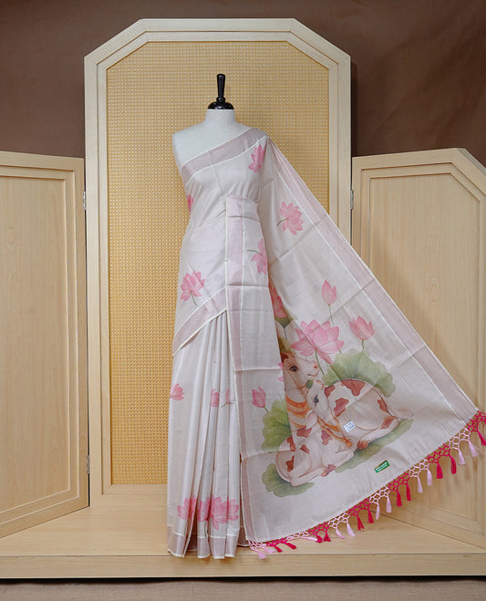 Cream Colour Tissue Kerala Saree Featuring Delicate Digital Lotus Prints And A Charming Cow & Calf Pallu, Enhanced With A Subtle Tissue Border And Contrast Pink Tassels. Paired With A Matching Blouse Piece.