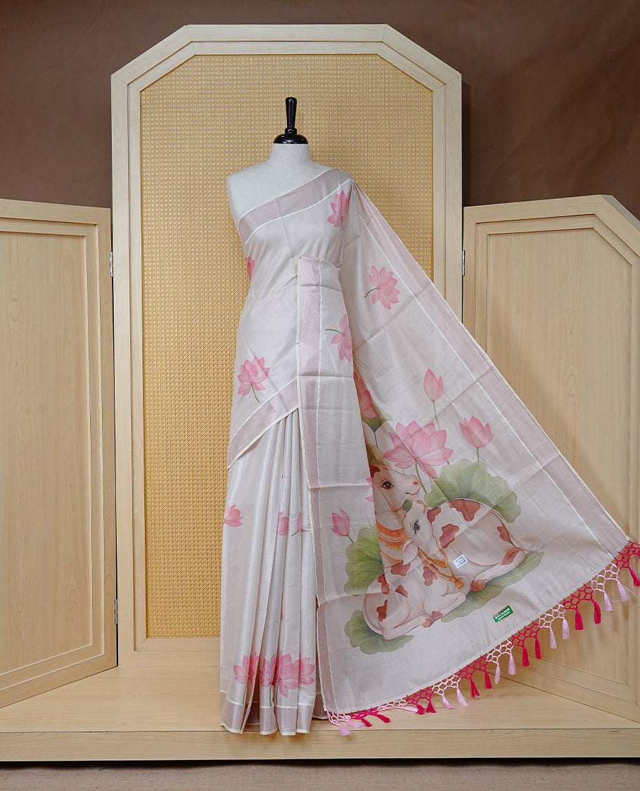 Cream Colour Tissue Kerala Saree Featuring Delicate Digital Lotus Prints And A Charming Cow & Calf Pallu, Enhanced With A Subtle Tissue Border And Contrast Pink Tassels. Paired With A Matching Blouse Piece.