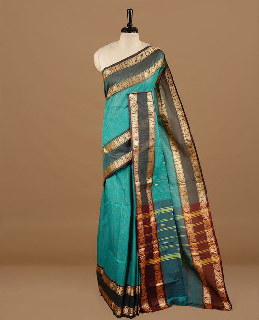 Teal colour chettinad cotton saree featuring gold zari motifs & check pattern on body, complemented by green colour with zari border, paired with matching blouse piece.
