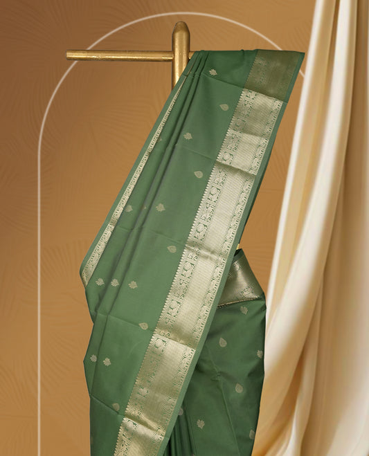 Dark pista green colour soft silk saree adorned with small golden buttas, enhanced by a shimmering gold zari border and pallu with delicate motifs & Paired with a matching blouse.