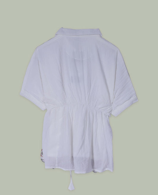 White three-quarter sleeve tunic top with round neckline and front yoke featuring teal and green floral embroidery with tie-up detail at the neck.