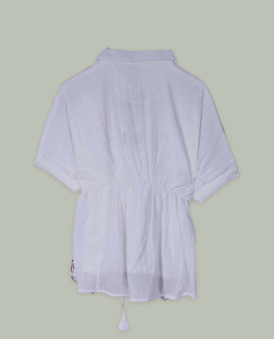 White three-quarter sleeve tunic top with round neckline and front yoke featuring teal and green floral embroidery with tie-up detail at the neck.