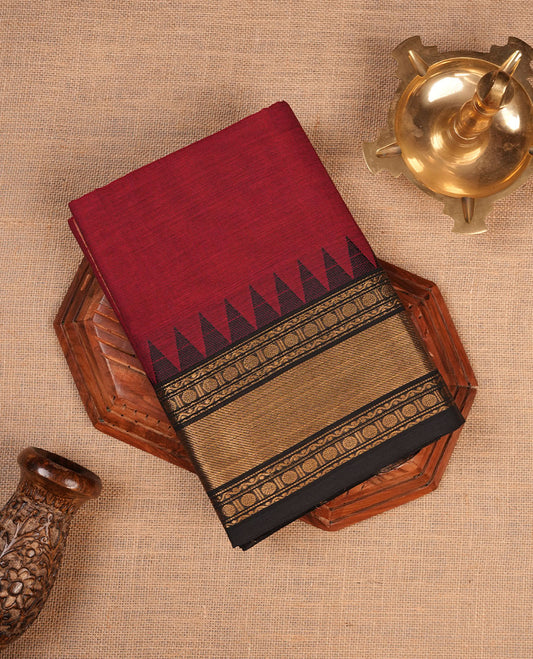Deep red colour chettinad cotton saree featuring elegant plain body highlighting contrast black colour with gold zari traditional border, pallu and paired with matching blouse piece.