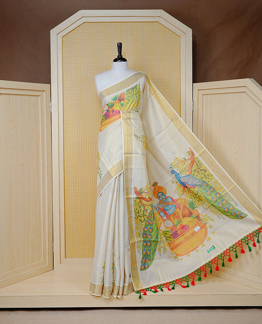 Cream Colour Tissue Kerala Saree Featuring A Digital Vishu Theme At Body & Pallu, Beautifully Enhanced With A Classic Gold Zari Border And  Green & Red  Tassels Paired With A Matching Blouse Piece.