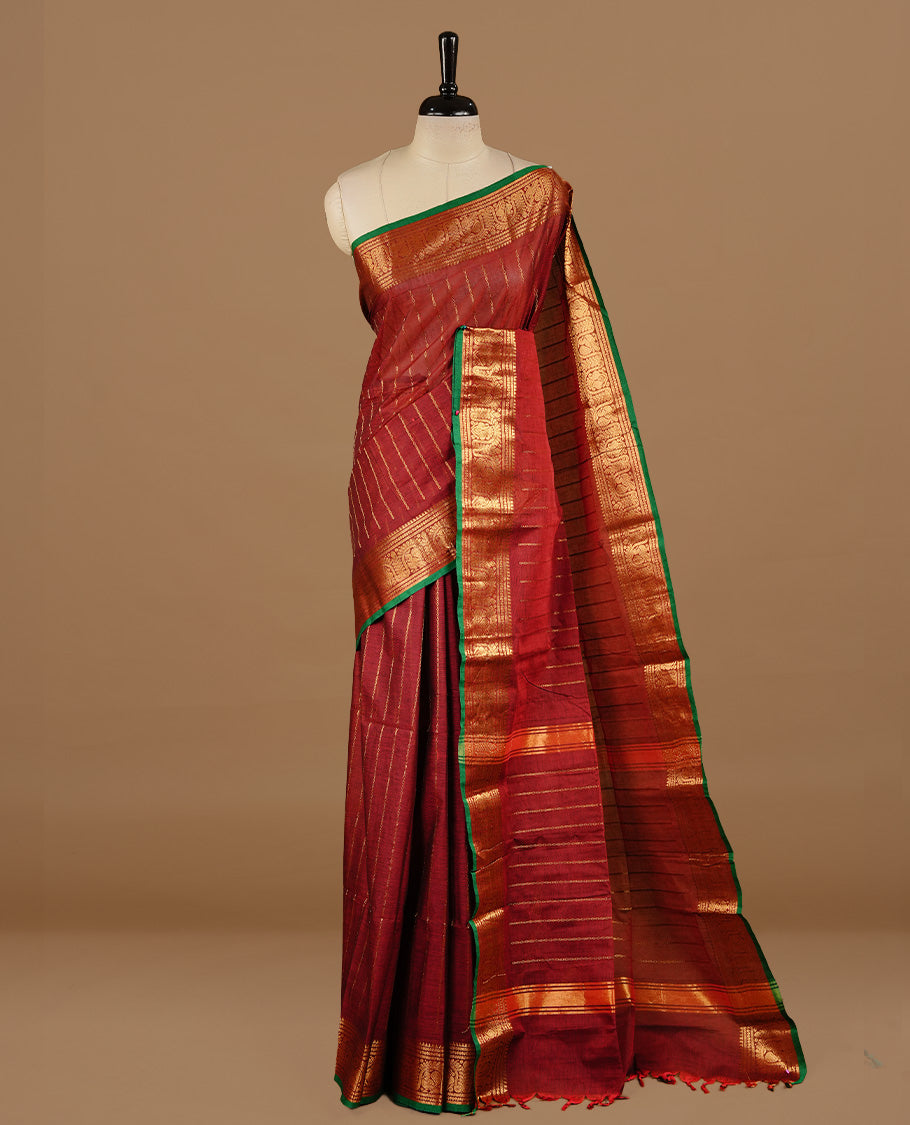 Maroon colour chettinad cotton saree featuring gold zari stripes on body, complemented by  self colour with zari green colour piping border, paired with matching blouse piece.