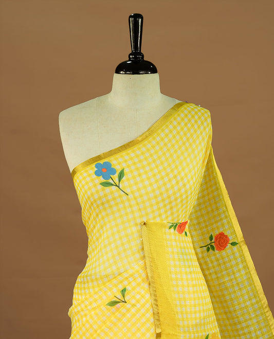 Yellow colour Semi Linen saree featuring a stylish check pattern adorned with floral prints on the body, enhanced by a small gold border, paired with a matching blouse piece.