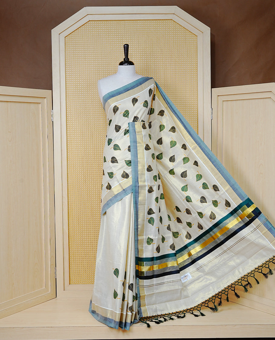 Cream Colour Tissue Kerala Saree Featuring Green and Black Leaf Prints Across the Body, Enhanced with a Gold Zari, Dark Green and Black Border & Pallu, Green  and Black Tassels, and a Matching Blouse Piece.