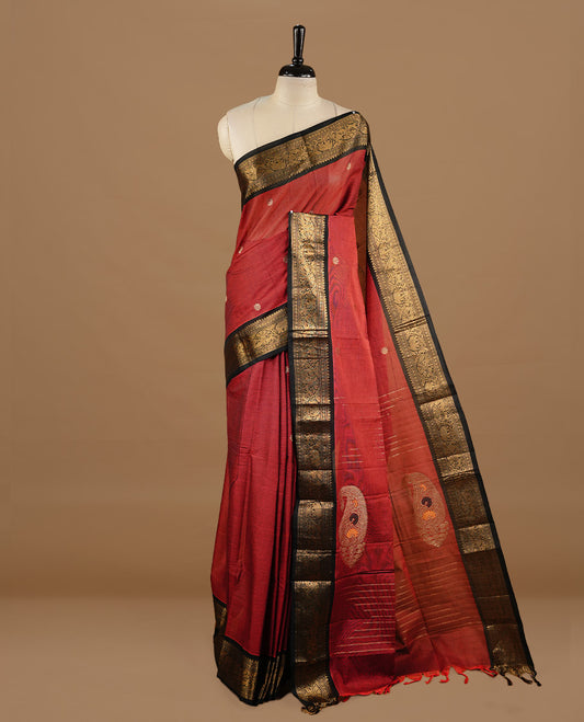 Dark red colour chettinad cotton saree featuring gold zari motifs on body, complemented by black colour with zari border, paired with matching blouse piece.