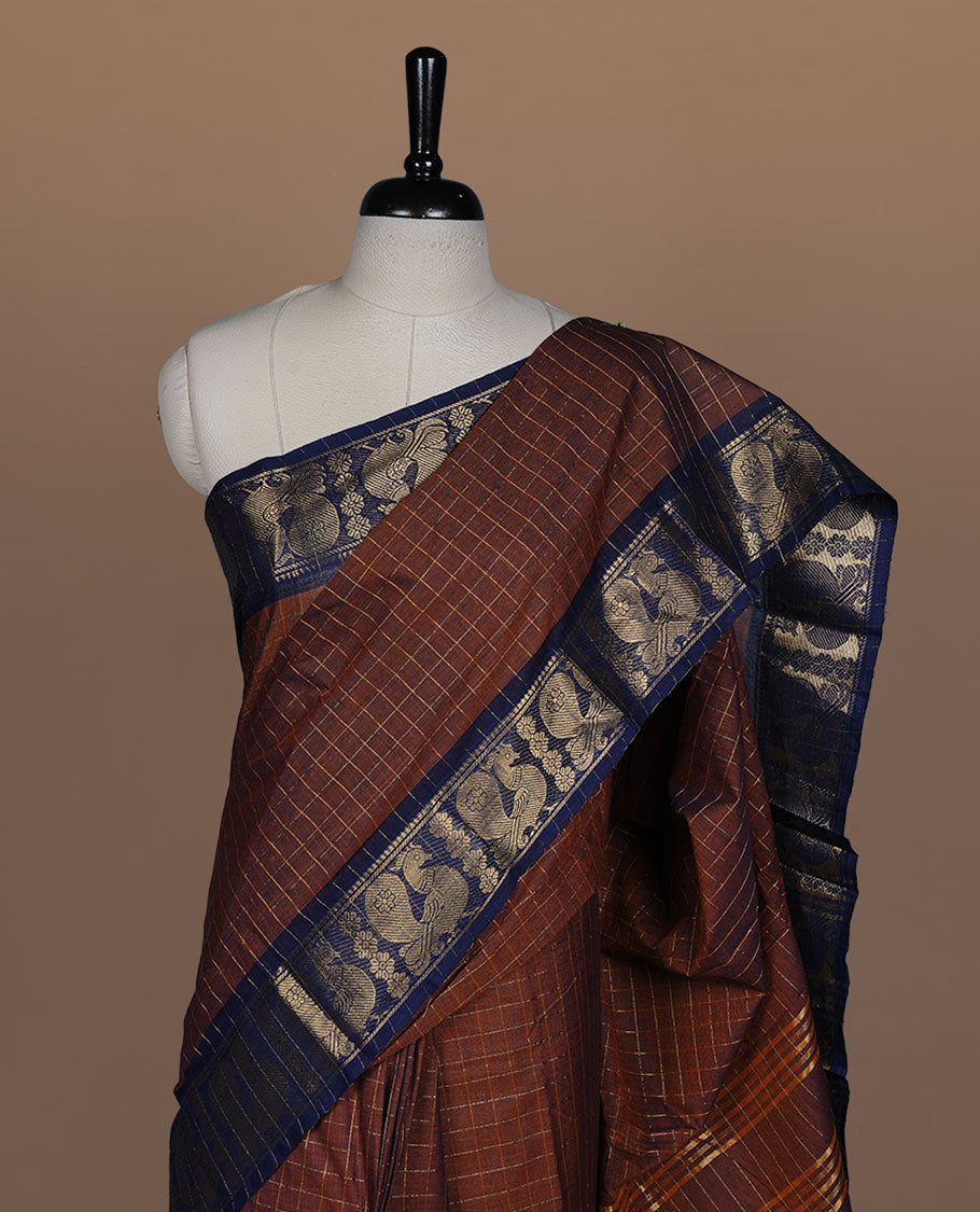 Brown colour sungudi cotton saree featuring gold zari check pattern across body, contrast Dark blue colour with gold zari peacock and floral pattern on border, without blouse piece.