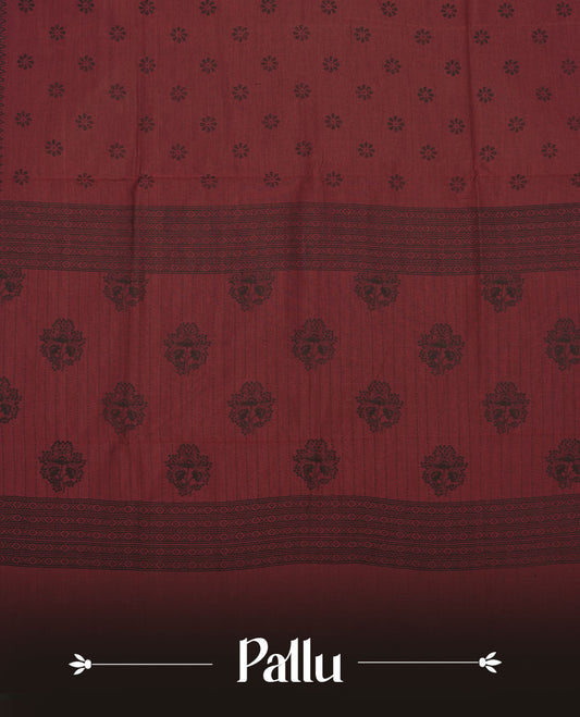 Deep maroon colour poly cotton saree with black floral butti motifs on the body, paired with a matching pallu featuring black ornate floral jaal and stripes on the border, and a coordinated all‑over black paisley printed blouse piece.