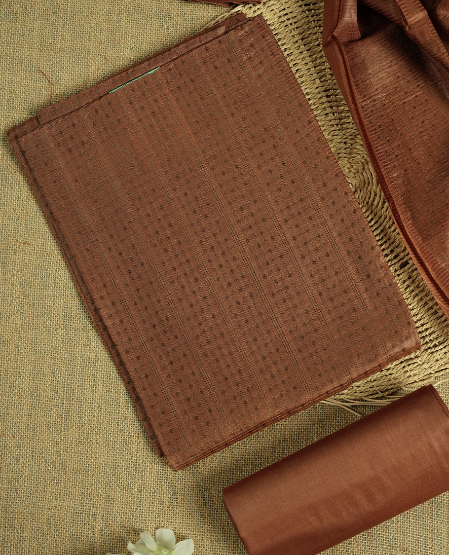Deep brown colour tussar suit material featuring a subtle self copper zari woven motifs and vertical and stripped pattern on the body, paired with a lightweight matching dupatta with tassel edges and a plain bottom piece.