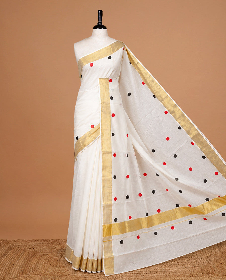 Cream Colour cotton Kerala Saree Featuring  Black & Red Dot Prints On The Body, Complemented By A Traditional Gold Zari Border, Paired With A Matching Blouse Piece.