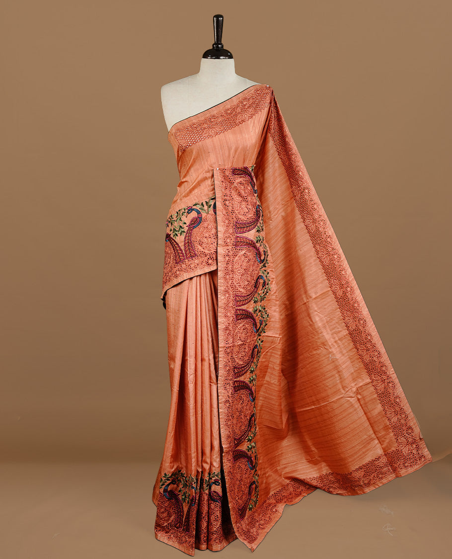 Peach colour Semi Tussar silk saree features an intricate cutwork embroidered peacock motifs on border, paired with a matching unstitched blouse piece.
