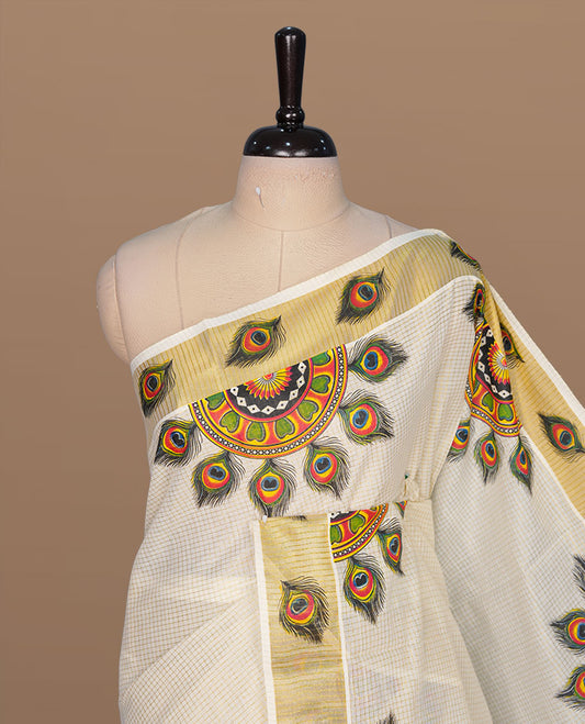 Off white color kerala cotton saree featuring gold zari check on body, complemented by, gold zari with peacock leaf printed border, paired with matching blouse piece.