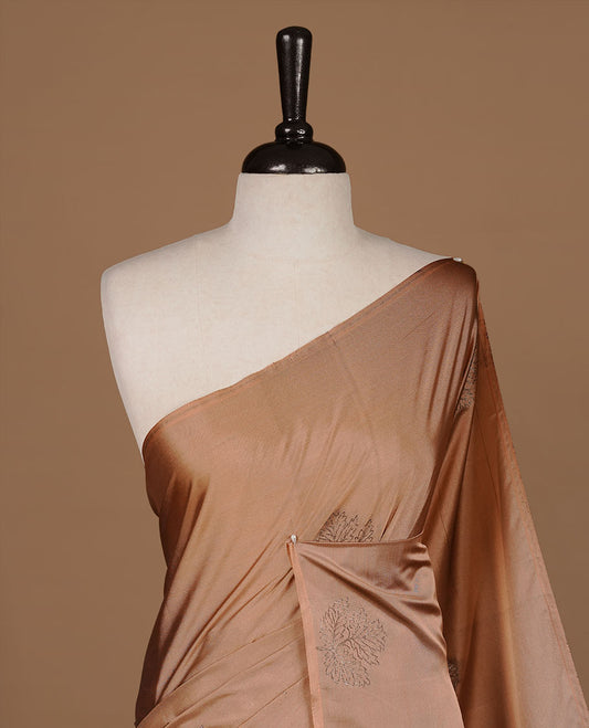 Dusty orange soft silk saree features a sleek borderless design with intricate antique zari motifs, flowing into a seamless self colored pallu and a matching blouse piece.