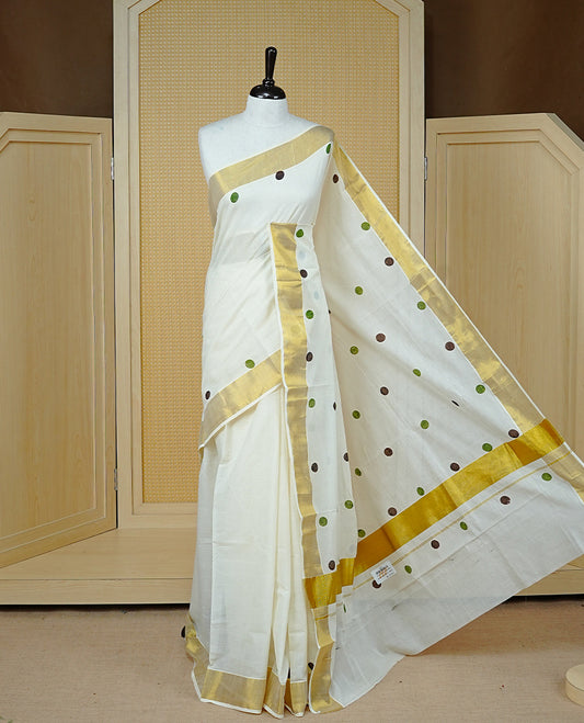 Cream Colour cotton Kerala Saree Featuring Multicolour Dot Prints On The Body, Complemented By A Traditional Gold Zari Border, Paired With A Matching Blouse Piece.