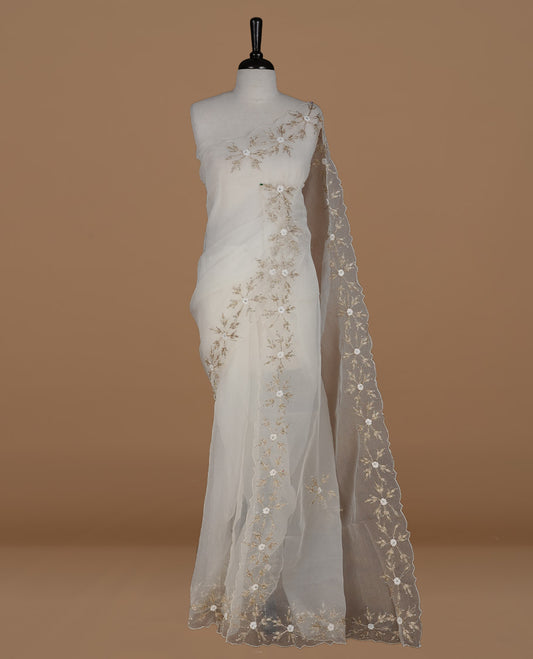 White colour crush organza saree featuring gold threan floral and stone worked body, highlighting scalp designed border, paired with matching blouse piece.