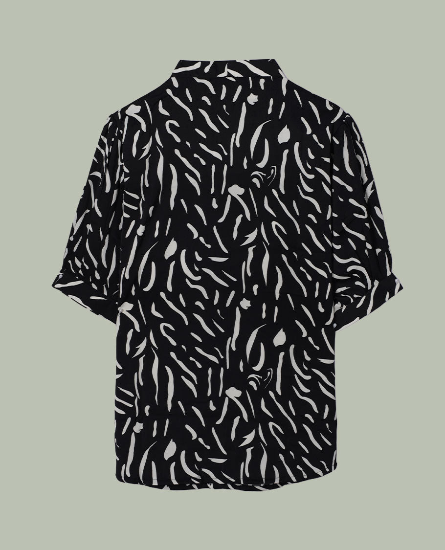 Black short-sleeve shirt top with collared neckline and all-over white abstract dash print, shown from the back.