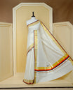 Cream colour cotton Kerala saree Featuring Gold zari Checks across the body, complemented by Classy gold zari with an orange & black Border & pallu, paired with a matching blouse piece.