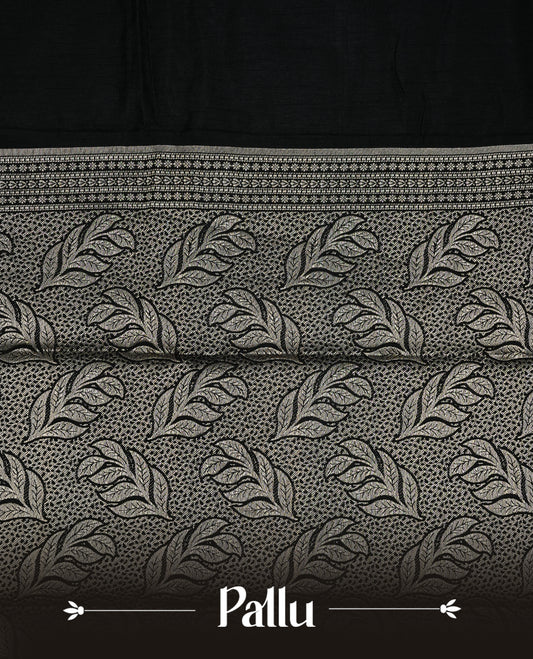 Black colour semi Tussar silk saree featuring an elegant plain body, complemented by a self colour border adorned with traditional gold zari floral kodi patterns. Comes paired with a matching blouse piece.