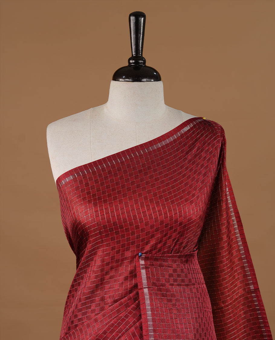 Maroon colour Semi Tussar saree featuring an elegant zari fancy check pattern on the body, highlighted with a small border for a refined look. Comes without a blouse piece.