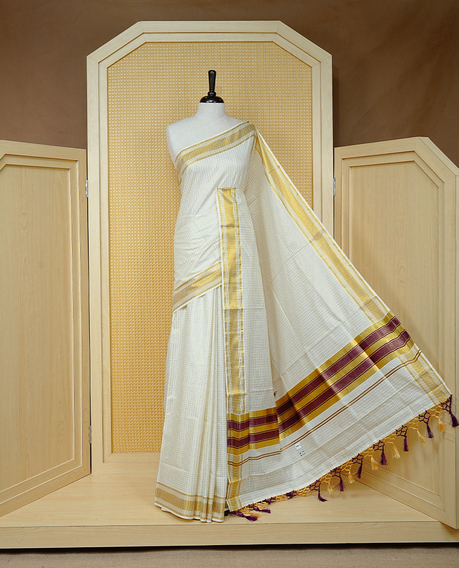 Cream colour Cotton kerala saree featuring Gold zari Checks on body, complemented by Gold zari border & Purple with gold zari on Pallu, paired with matching blouse piece.