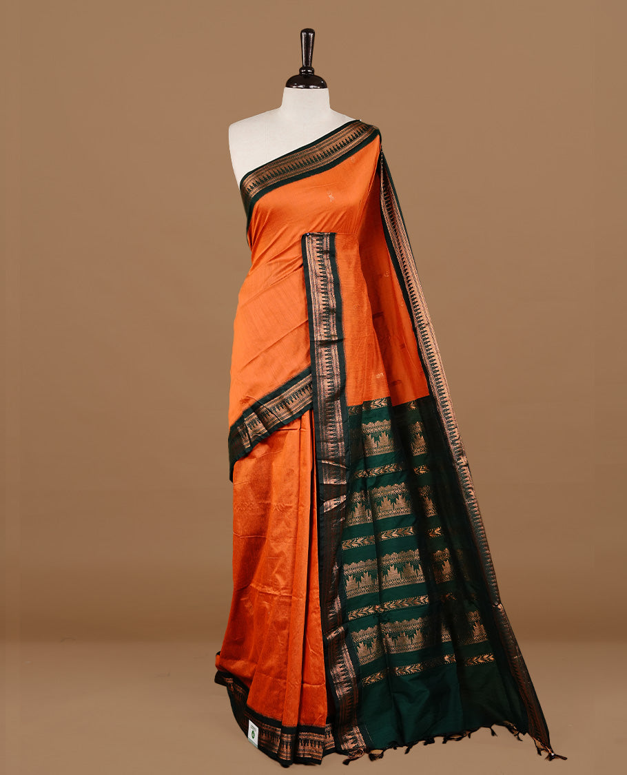 Orange colour kalyani cotton saree featuring gold zari motifs on body, highlighting contrast green colour with Antique gold zari border, paired with matching blouse piece.