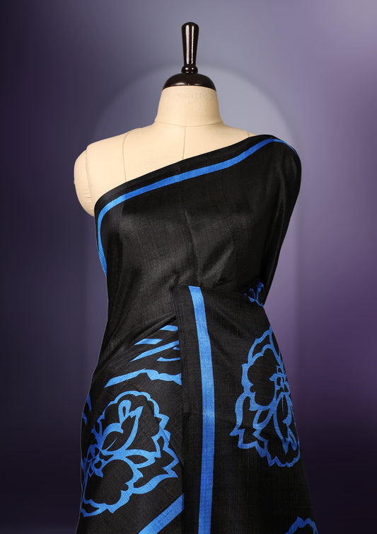 Elegant black colour art silk saree with bold blue floral prints and matching border & Accentuated with a tassel detailed pallu, its perfect for festive evenings or parties. Comes with an unstitched blouse piece.