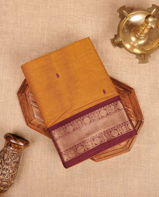 Mustard Brown colour chettinad cotton saree featuring plain body, paired with a black colour traditional gold zari border paired with matching blouse.