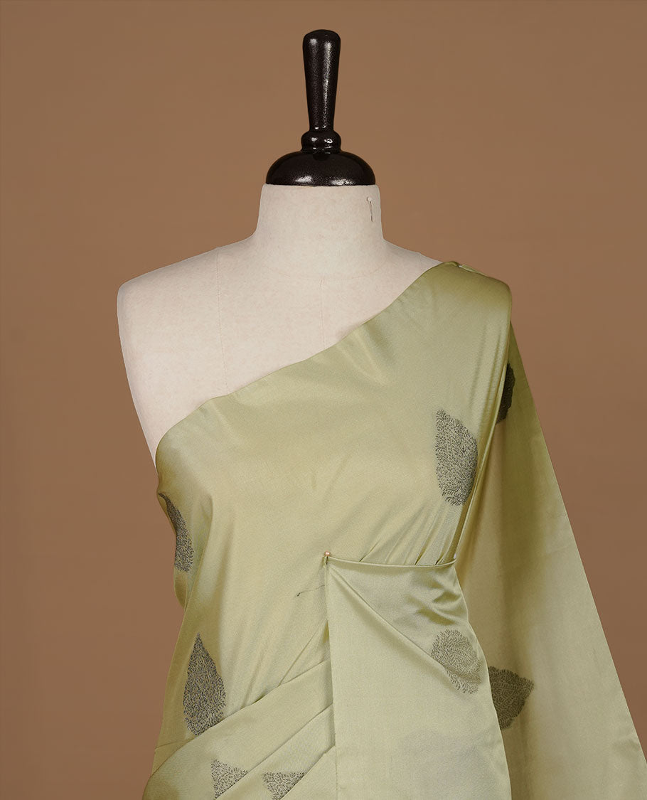Tea green soft silk saree features a sleek borderless design with intricate antique zari motifs, flowing into a seamless self colored pallu and a matching blouse piece.