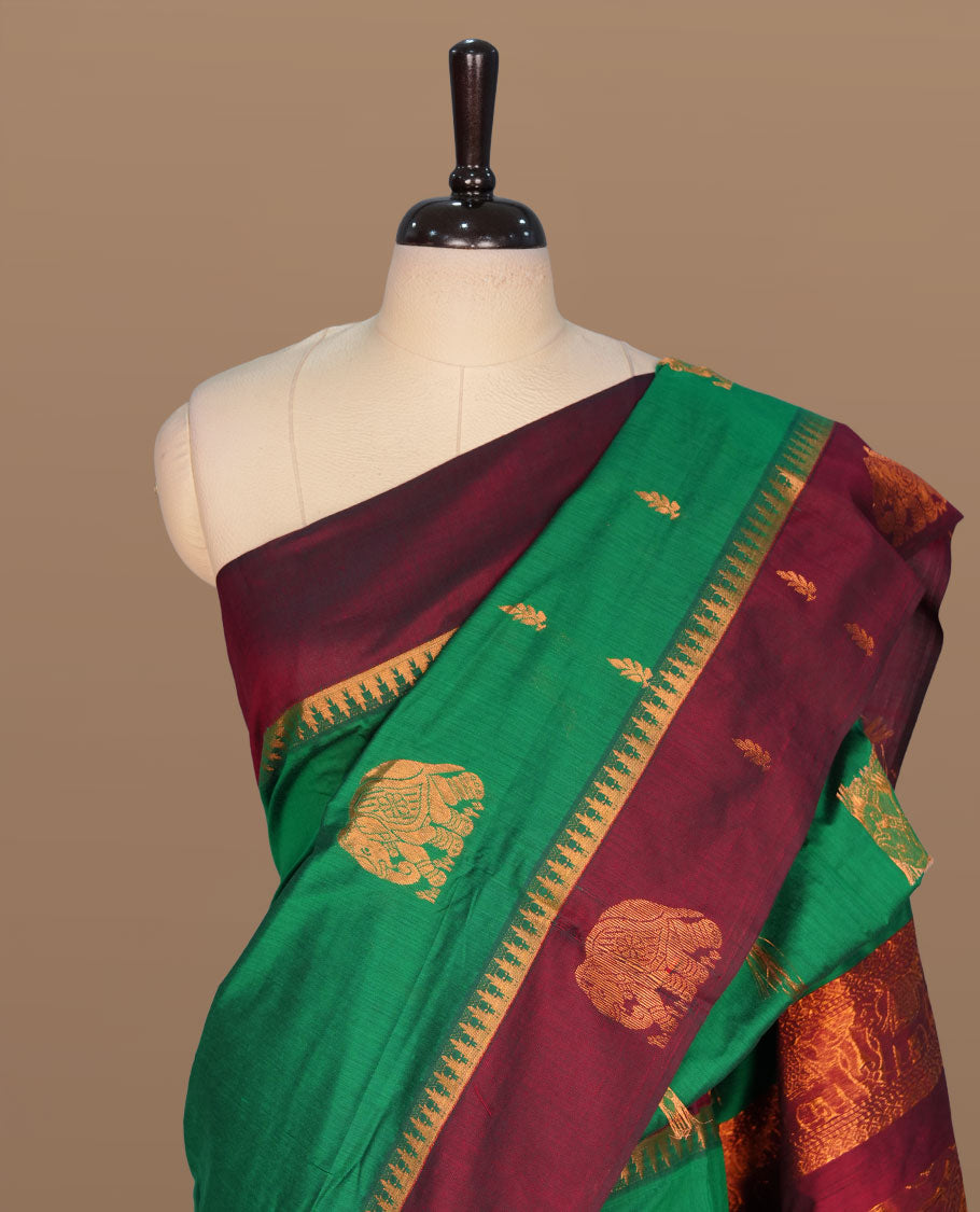 Green colour kalyani cotton saree featuring gold zari motifs on body, complemented by contrast maroon color with copper zari elephant pattern border , paired with matching blouse piece.